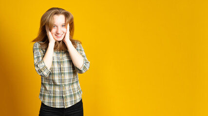 Banner copy space. Pretty young girl, with long hair, laughs, shows a beautiful smile, dressed in a plaid shirt, on a yellow background.