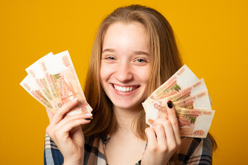 Happy young woman holding Russian rubles, received a scholarship, a salary on a yellow background. Finance concept.
