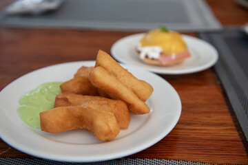 Chinese bread stick, a deep fried Chinese donut, a popular Chinese breakfast served on a white plate with condensed milk. All placed on wooden table in modern restaurant in resort for breakfast.