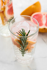 Glass of tasty grapefruit lemonade with rosemary on light background, closeup