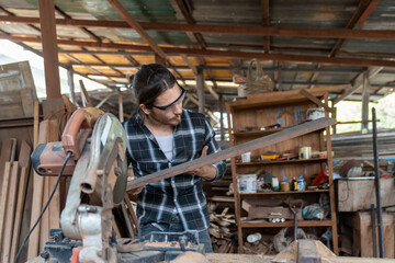 Fototapeta premium Male carpenter using circular saw cutting piece of wood and wearing safety goggles at woodwork workshop. Male woodworker working at work. Professional male craftsman