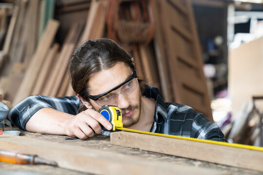 Male carpenter using measuring tape at the carpentry workshop. Joiner wearing safety goggles working with tape measure in his workplace © amorn
