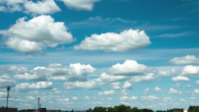 The movement of many small clouds over the rooftops. Video footage of a beautiful clear sunny blue sky with white fluffy clouds. The clouds move from left to right
