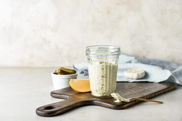 Glass with tasty tartare sauce, lemon and pickled cucumbers on light background