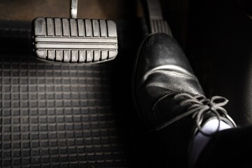 A man in leather shoes is stepping on the accelerator of a car.