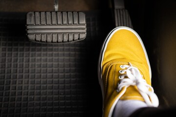 A man in yellow sneakers is stepping on the accelerator of a car. - obrazy, fototapety, plakaty