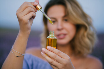 Fototapeta premium Woman holding bottle with natural essential oil in a lavender field.