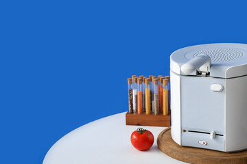 Modern deep fryer, tomato and spices on table near color wall