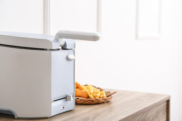 Modern deep fryer, tasty french fries and nuggets on table near light wall