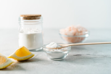 Eco friendly natural cleaners, jar with baking soda, lemon, pink salt and wooden spoon on marble table background. Organic ingredients for homemade cleaning. Zero waste concept.