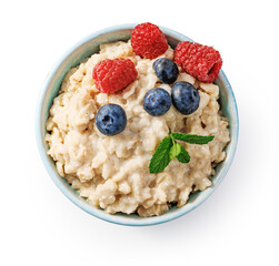 Oatmeal porridge with blueberries and raspberries with fresh mint in blue bowl. Porridge isolated on white background. Top view flat lay. Bowl of porridge for package design.