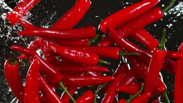 Super Slow Motion Shot of Flying Fresh Chilli Peppers and Water Side Splash Isolated on Black at 1000 fps.