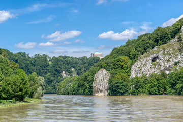 Fototapeta na wymiar View of the Danube river near the town of Kelheim (Germany) on a summer day. At the top of the mountain is the majestic Hall of Liberation (Befreiungshalle). On the banks are massive rocks 