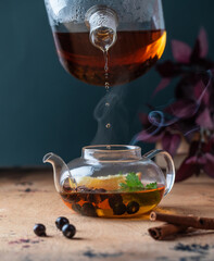 A teapot with black tea with currant berries, lemon, a cinnamon stick. Autumn background. 
