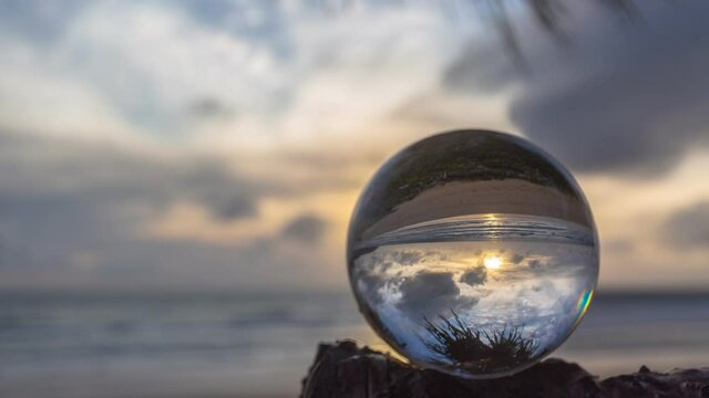 ..view on the beach in beautiful sunset inside crystal ball placed on a branch shaking while windy. .time lapse Unconventional and beautiful natural views on the beach inside a magic crystal ball. .