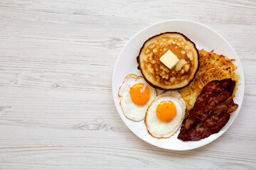 Full American Breakfast with Bacon, Hash Browns, Eggs and Pancakes on a plate on a white wooden background, top view. Space for text.