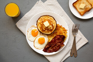 Full American Breakfast with Bacon, Hash Browns, Eggs and Pancakes on a plate on a gray surface, top view. Flat lay, overhead, from above.