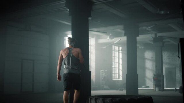 Guy getting up from rubber tire. Man with hammer finishing crossfit workout