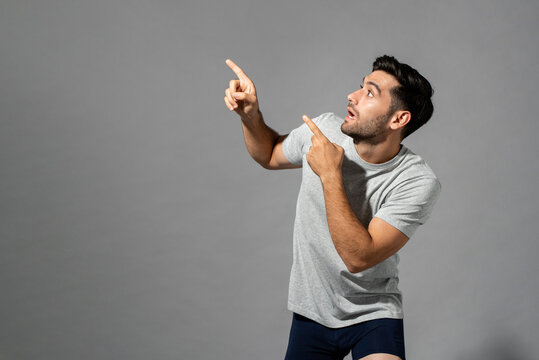 Shocked young Caucasian man with hands pointing up in isolated light gray studio background