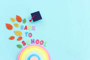 Back to school concept. Top view image of rainbow memo paper, graduation hat and text over blue...