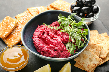 Composition with tasty beet hummus, crackers, olives and sauce on dark background, closeup