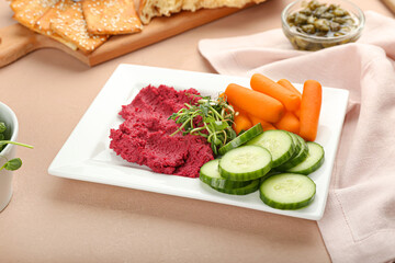 Plate with tasty beet hummus, carrots and cucumbers on color background