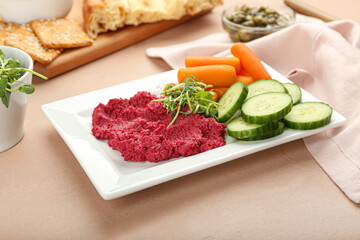 Plate with tasty beet hummus, carrots and cucumbers on color background