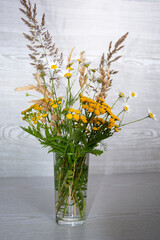 A bouquet of wildflowers in a glass vase on a wooden background.