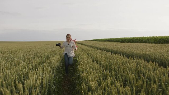 Smiling girl running in the green-yellow wheat filed