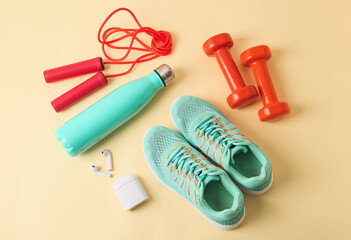 Sport shoes, earphones and equipment on color background