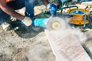 Hands of a pavement construction worker using an angle grinder for cutting the tiles