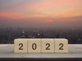 2022 letter on block cubes on wooden table over blur of cityscape on warm light sundown, Happy new...