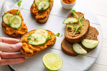 Female hand with tasty bruschettas on white wooden background