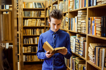Thin guy in blue shirt reading a book with interest. Student in the library, university, college...