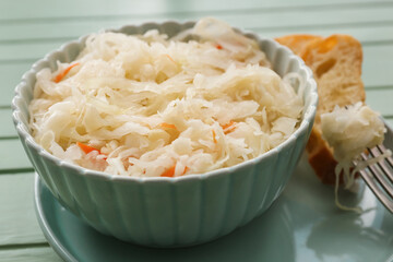 Bowl with tasty sauerkraut and fresh bread on color wooden background