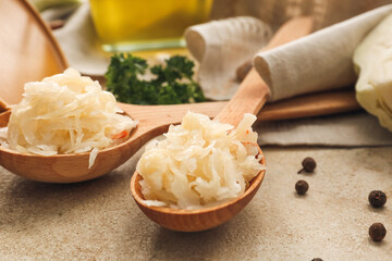 Spoons with tasty sauerkraut on grunge background, closeup