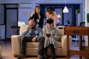 Diverse team of people use vr glasses on tv console at office party celebration after work. Multi ethnic colleagues play with joystick controller having fun enjoyment entertainment