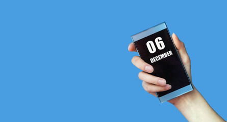 december 06. 06th day of the month, calendar date.Woman's hand holds mobile phone with blank screen on blue isolated background.Winter month, day of the year concept