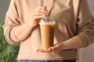 Woman holding plastic cup with tasty iced coffee indoors, closeup