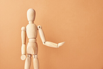 Wooden doll with gesture on pastel beige background. Mannequin shows gesture. Figure of wooden human with copy space