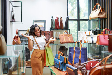 Portrait of happy shopaholic smiling at camera while choosing and buying bags for herself in the shopping mall