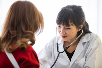 Doctor with long black hair white lab coat sitting checking heartbeat of lady who has blond hair...