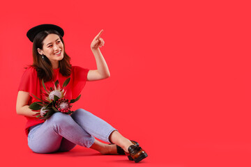 Beautiful young woman with protea flowers pointing at something on color background