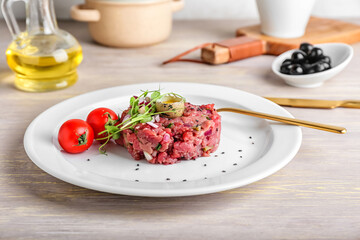 Plate with tasty beef tartare on light wooden table