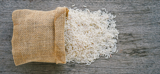 Organic raw rice spilling from small burlap sack bag on wood desk background 