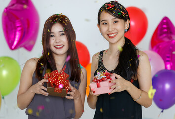 Delighted Asian girlfriends standing under confetti