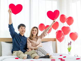 Cheerful Asian couple showing paper hearts on bed