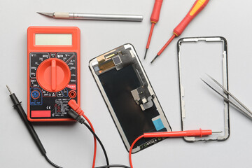 Disassembled mobile phone with technician tools on grey background