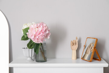Vase with hydrangea flowers and decor on mantelpiece near light wall