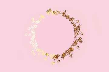 Round frame made of gold colored stars confetti on a pink pastel background.